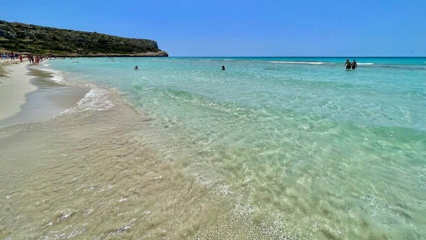 A beach with clear turquoise water, a sandy shore, and a rocky outcrop in the background. - SUITE CON VISTAS A PLAYA DE SON BOU (Son Bou (Platja))