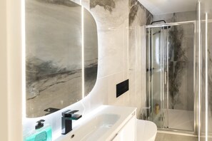 A modern bathroom with a marble wall, a glass shower enclosure, and a white sink. - MADRID. SL21 VacaHome Management (Madrid)