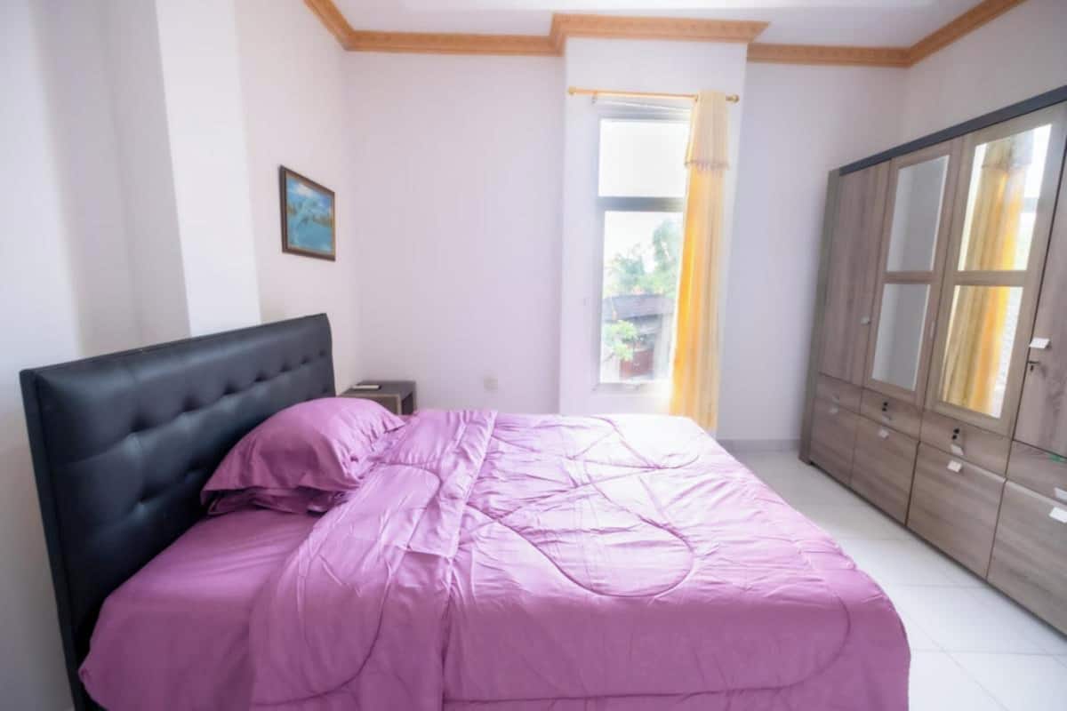A bedroom with a bed, a wardrobe, a nightstand, and a window with curtains.