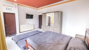 A bedroom with two beds, a wardrobe, a television, and a door. - Hotel Mega Dana (Denpasar)