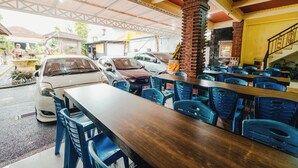 A restaurant with outdoor seating, cars parked outside, and a staircase leading to an upper level. - Hotel Mega Dana (Denpasar)