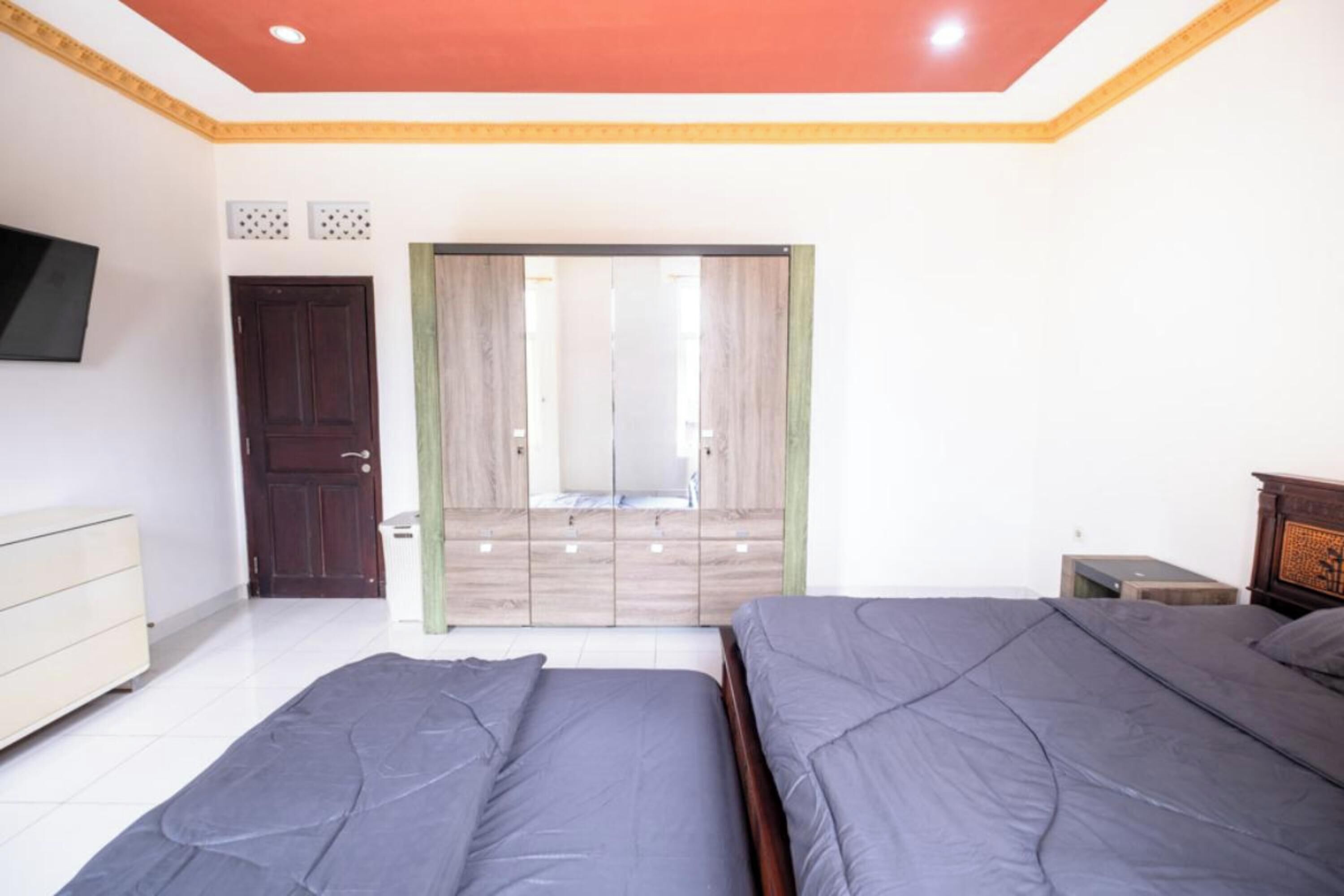A bedroom with two beds, a wardrobe, a television, and a door leading to another room.