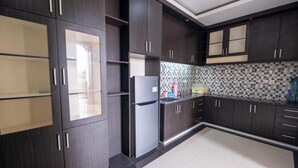 A modern kitchen with dark wood cabinets, a stainless steel refrigerator, and a tiled backsplash. - Hotel Mega Dana (Denpasar)