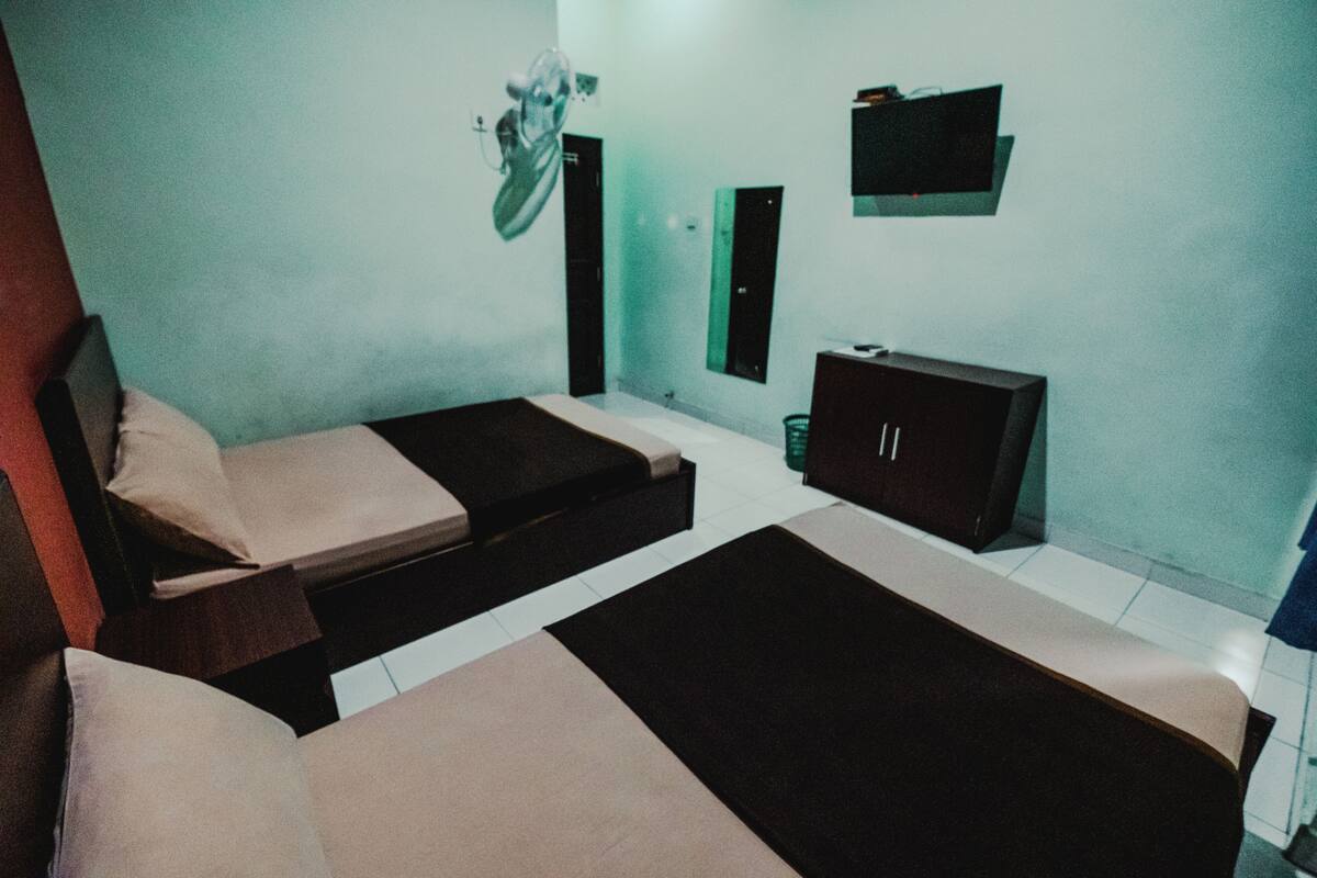 A room with two beds, a small cabinet, and a mirror on the wall.