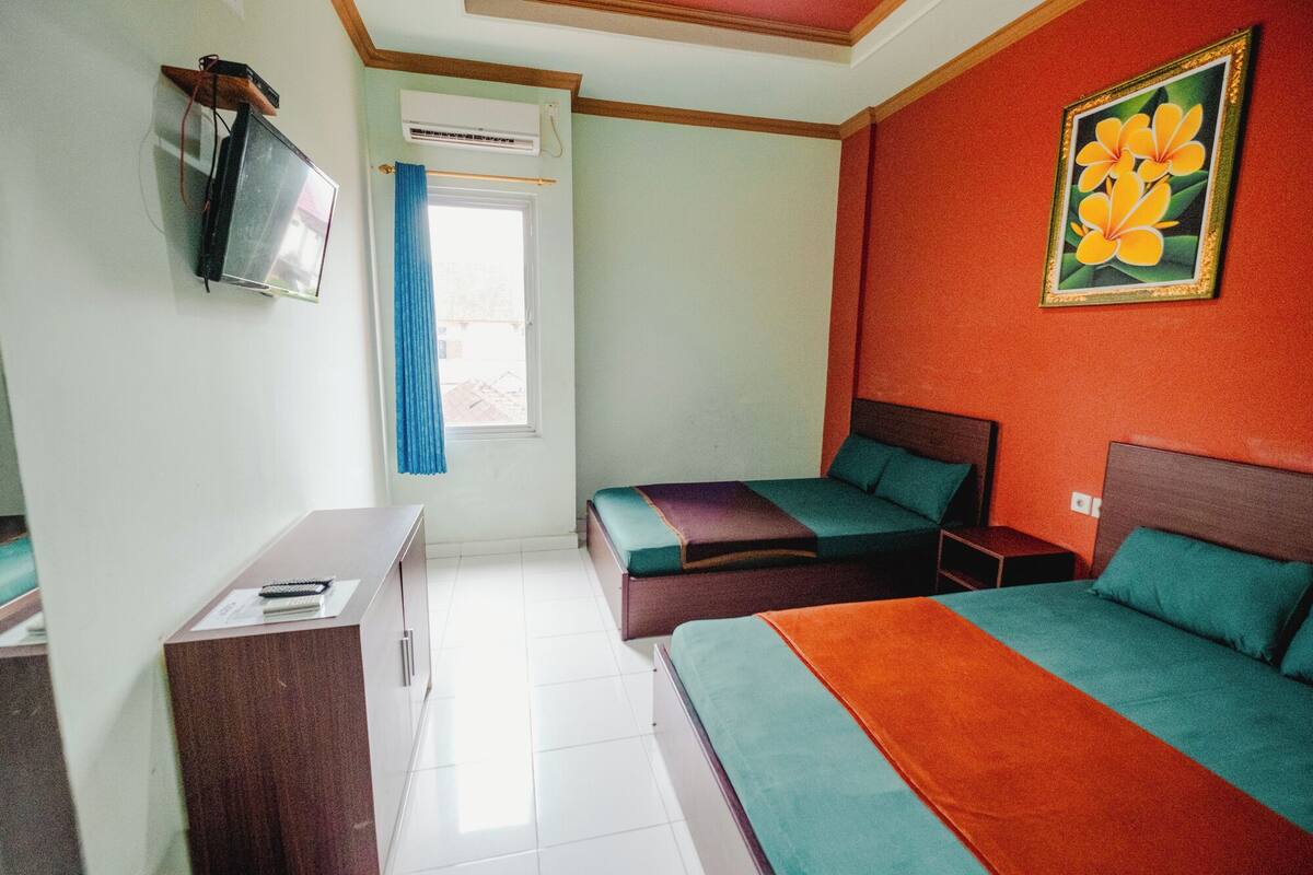 A hotel room with two beds, a desk, a TV, and a window with curtains.