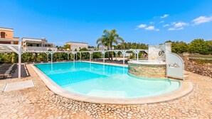 Een zwembad met een terras van stenen tegels, een jacuzzi en een pergola.