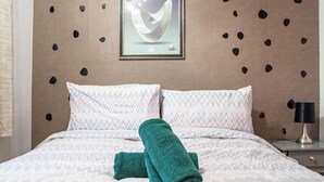 A neatly made bed with patterned bedding, a green towel, and a wall with a geometric design. - Welcome to Agape Apartment! Family- Friendly. CALLED HOME AWAY FROM HOME (Lowedges)