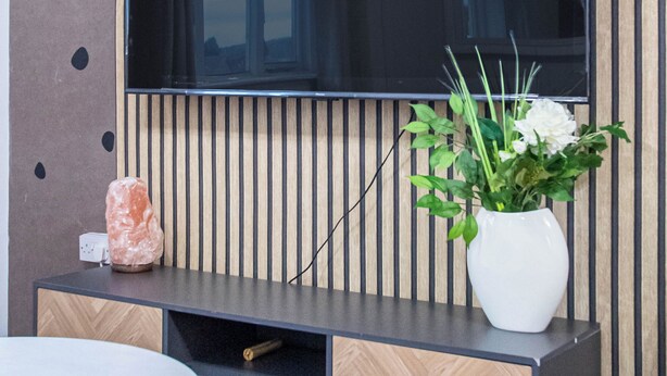 A modern living room with a large flat-screen TV mounted on a wall with vertical wooden slats. - Welcome to Agape Apartment! Family- Friendly. CALLED HOME AWAY FROM HOME (Lowedges)