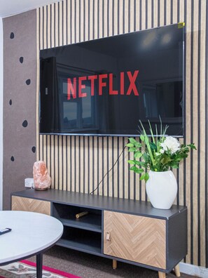 Uma sala de estar moderna com uma televisão de tela grande fixada em uma parede com ripas de madeira verticais.