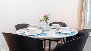 A round dining table with four black chairs, a vase with flowers, and matching tableware. - Welcome to Agape Apartment! Family- Friendly. CALLED HOME AWAY FROM HOME (Lowedges)