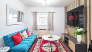 A modern living room with a blue sofa, a round coffee table, a TV mounted on the wall, and a decorative plant. - Welcome to Agape Apartment! Family- Friendly. CALLED HOME AWAY FROM HOME (Lowedges)