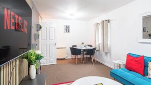 A modern living room with a blue sofa, a white coffee table, and a dining area with a white table and chairs. - Welcome to Agape Apartment! Family- Friendly. CALLED HOME AWAY FROM HOME (Lowedges)