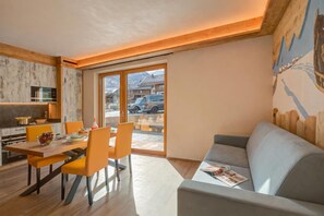 Une cuisine moderne avec des meubles en bois, une table à manger avec des chaises orange et un canapé gris dans un salon donnant sur la rue.