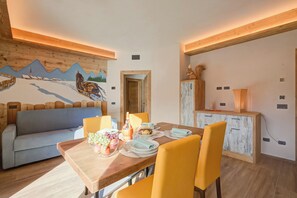 A dining area with a wooden table set for four, yellow chairs, and a painting of a snowy landscape on the wall. - Arnica Ski In 10 m, Livigno, Italy (Livigno)