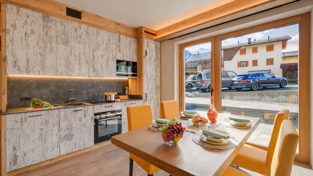 A modern kitchen with wooden cabinets, a dining table with chairs, and a view of the street through large windows. - Arnica Ski In 10 m, Livigno, Italy (Livigno)