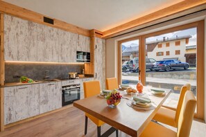 Una cocina moderna con armarios de madera, una mesa de comedor con sillas y vistas a la calle a través de amplios ventanales.