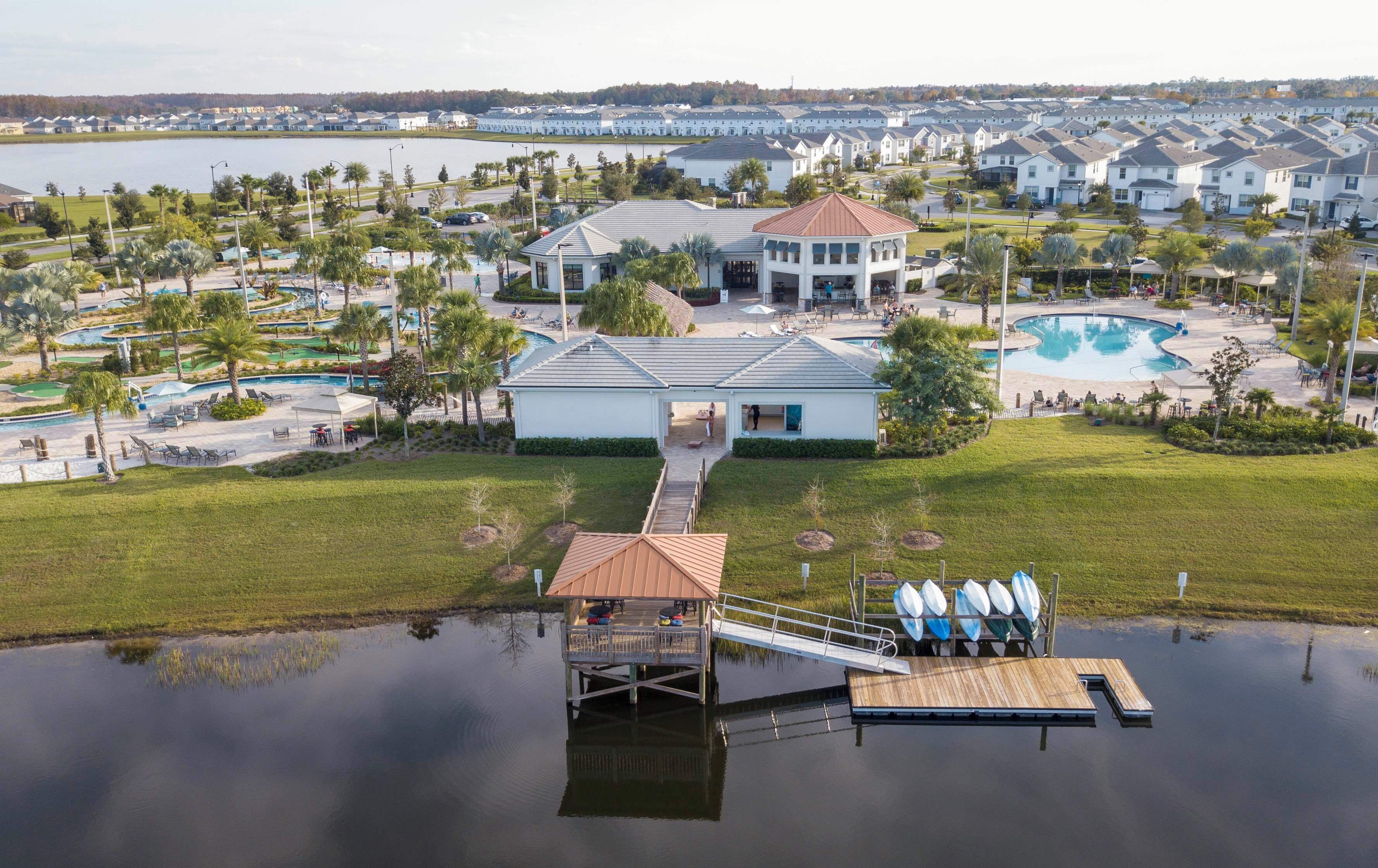 An aerial view of a residential area with a large swimming pool, a dock with surfboards, and a marina.