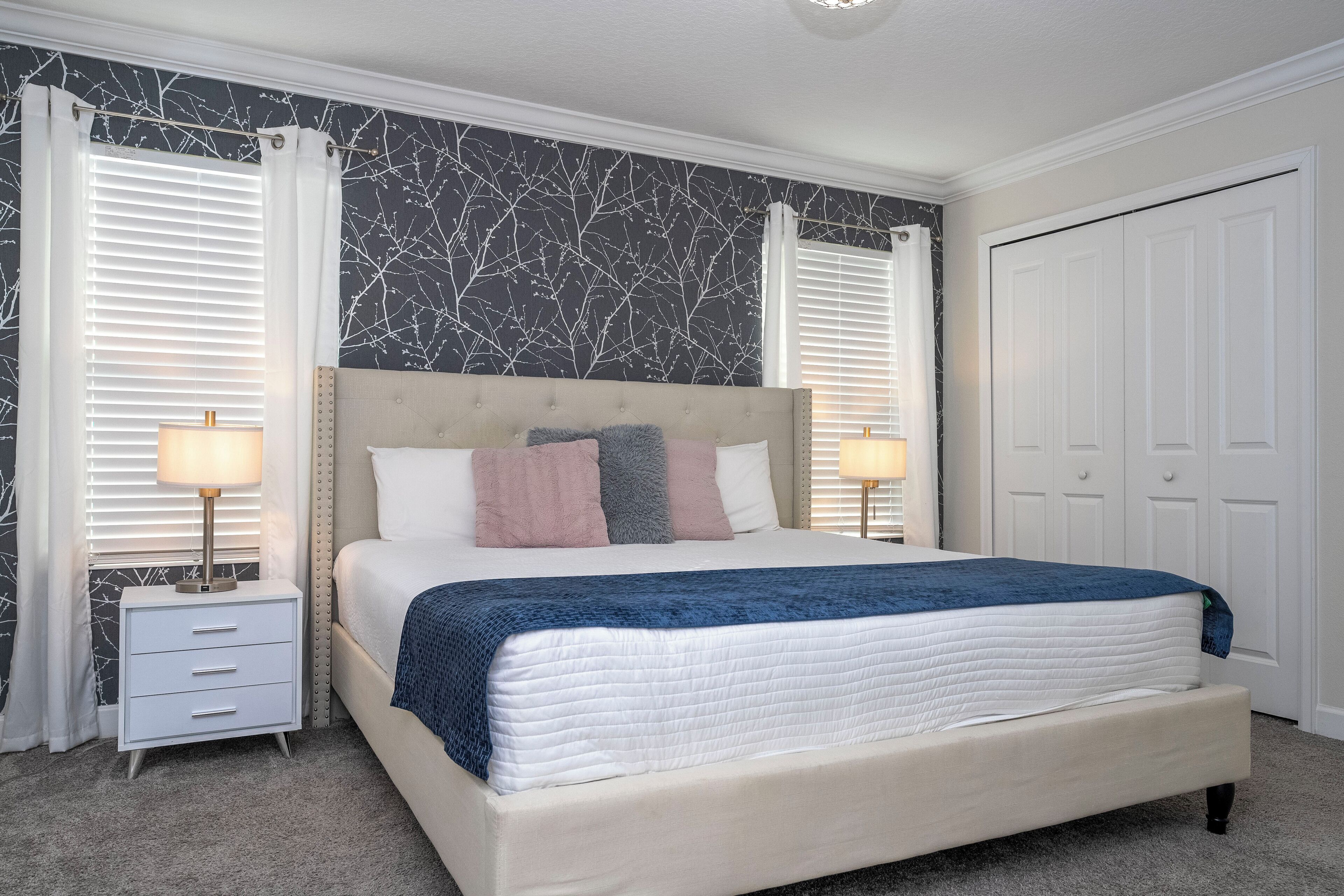Une chambre avec un grand lit, deux tables de chevet avec des lampes, une armoire et un mur orné d’un motif représentant une branche d’arbre.