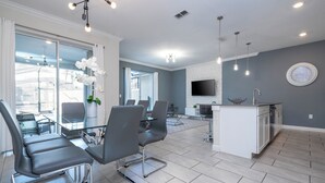 A modern kitchen with a built-in island, a dining area with a glass table and chairs, and a large window with curtains. - 4337 QS - Charming Hideaway (Kissimmee)