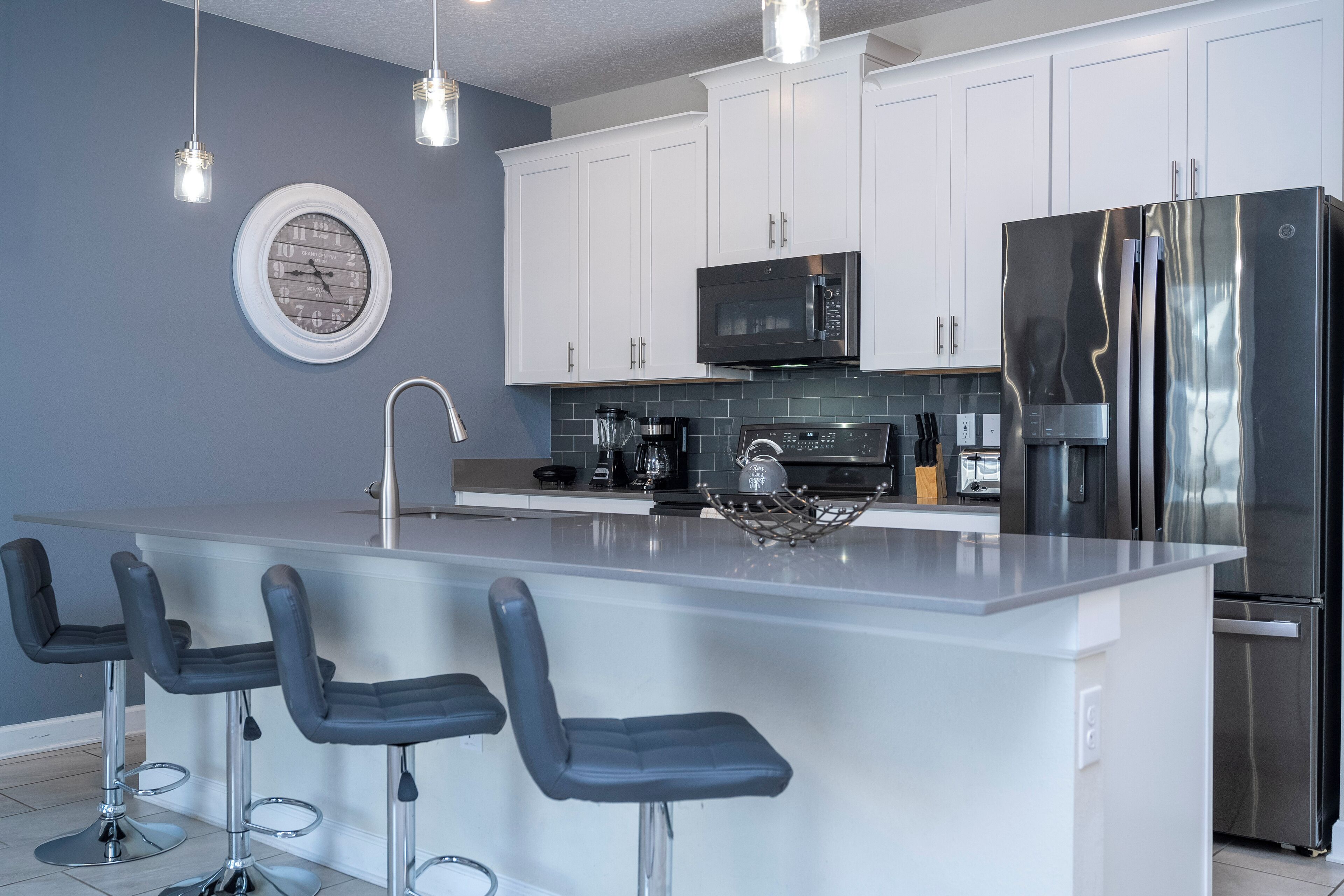 Una cocina moderna con armarios blancos, un refrigerador de acero inoxidable, un microondas y una isla grande con taburetes de bar.