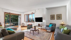 Ein geräumiges Wohnzimmer mit einer großen Couch, einem kleineren Sessel, einem Couchtisch und einem an der Wand befestigten Fernseher.