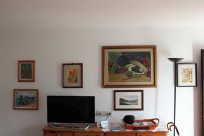 A living room with a flat-screen TV, framed artwork on the wall, and a wicker basket on a wooden table. - Suite Marco nice apartment  in Cavalese with View (Cavalese)