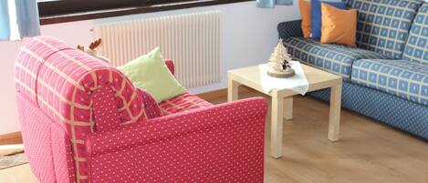 Una sala de estar con un sofá rojo, un sofá azul con estampado, una mesita de madera y un radiador.