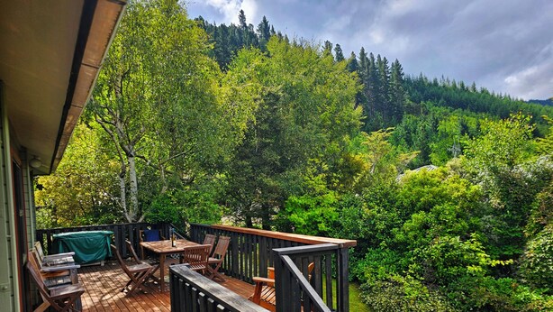 Une terrasse en bois, agrémentée de mobilier d’extérieur, entourée d’une végétation luxuriante et bordée d’une colline boisée.