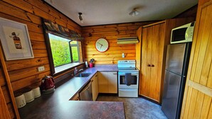 Une cuisine de taille réduite avec des murs en bois, un évier, une cuisinière et un réfrigérateur.