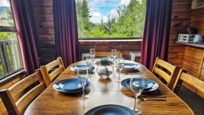 Une table de salle à manger en bois, dressée avec de l’argenterie bleue, des verres à vin et des couverts, et offrant une vue sur la verdure à l’extérieur.