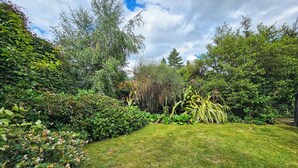 Un jardin luxuriant, avec une grande variété de plantes et d’arbres, une pelouse bien entretenue et un ciel dégagé.