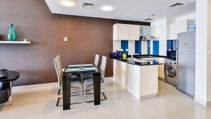 A modern kitchen with white cabinets, a central island, a washing machine, and a dining area with a table and chairs.