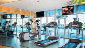 A modern gym with treadmills, ellipticals, and stationary bikes, large windows, and a TV screen.