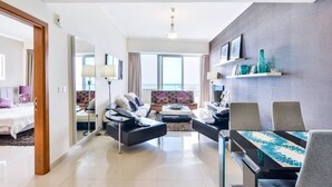 A modern living room with a sofa, coffee table, and dining area. There is a TV mounted on the wall and a window providing natural light.