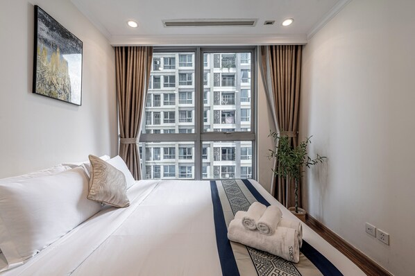 Habitación de hotel con un ventanal grande, una cama con ropa blanca, una alfombra estampada y una planta en maceta.