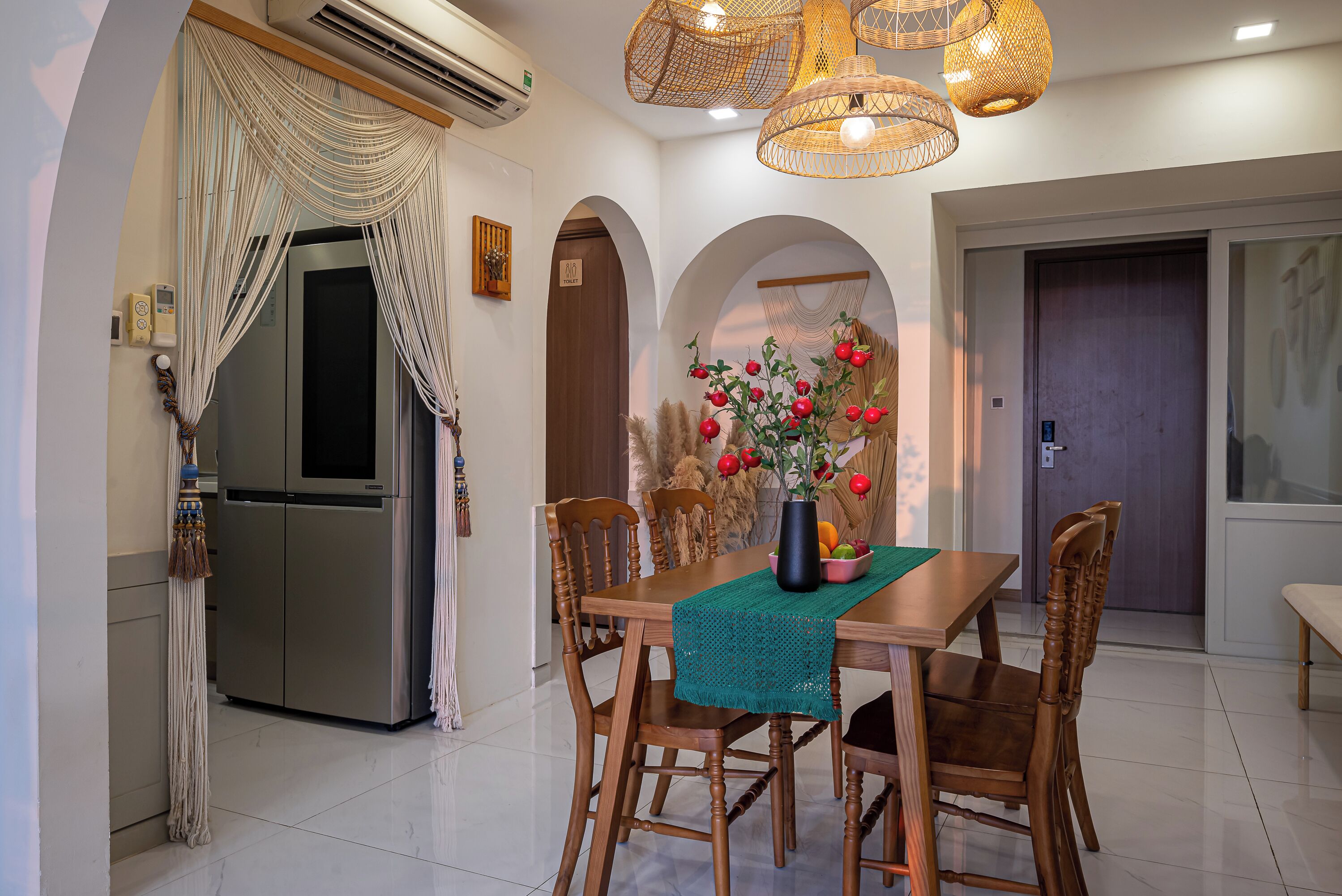 A dining area with a wooden table, chairs, and a vase of flowers. There is a refrigerator and a door in the background.