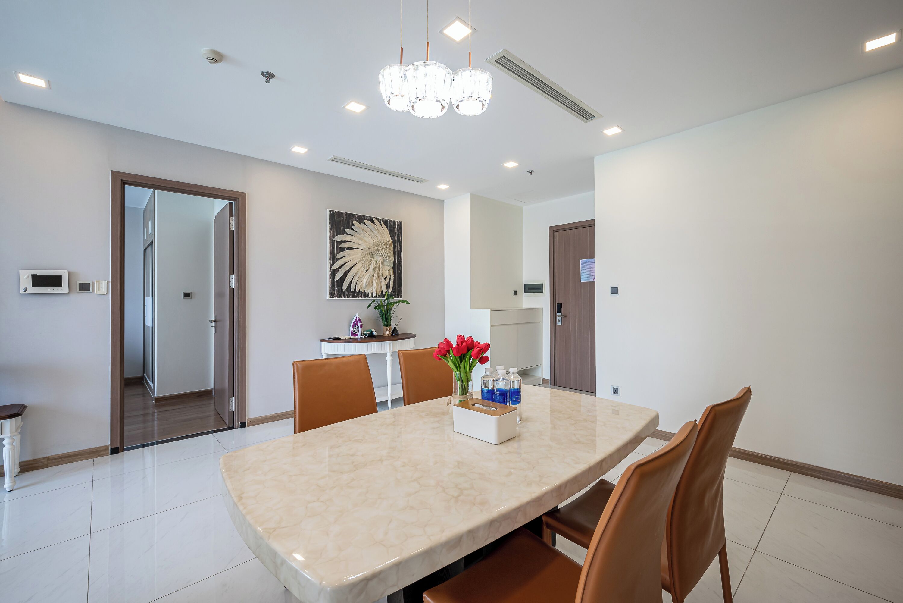 A modern dining area with a marble table, brown chairs, a chandelier, and a decorative wall piece.