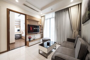 A modern living room with a flat-screen TV, a glass coffee table, and a grey sofa.