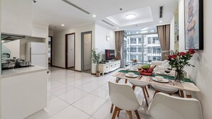 A modern kitchen with a dining area, a TV, and a view of the city. - Vinhomes Central Park Apartment by Hava (Ho Chi Minh City)