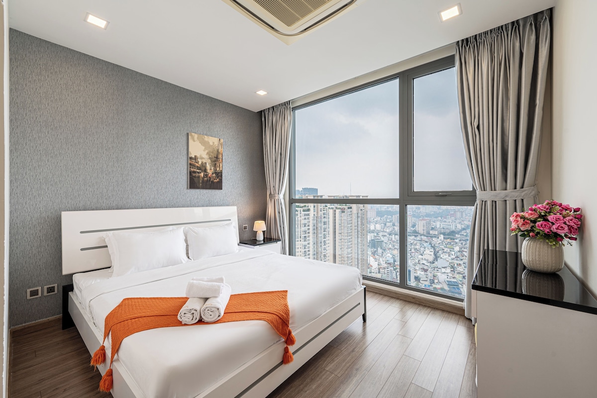 A modern hotel room with a large bed, a city view, and a window with curtains.