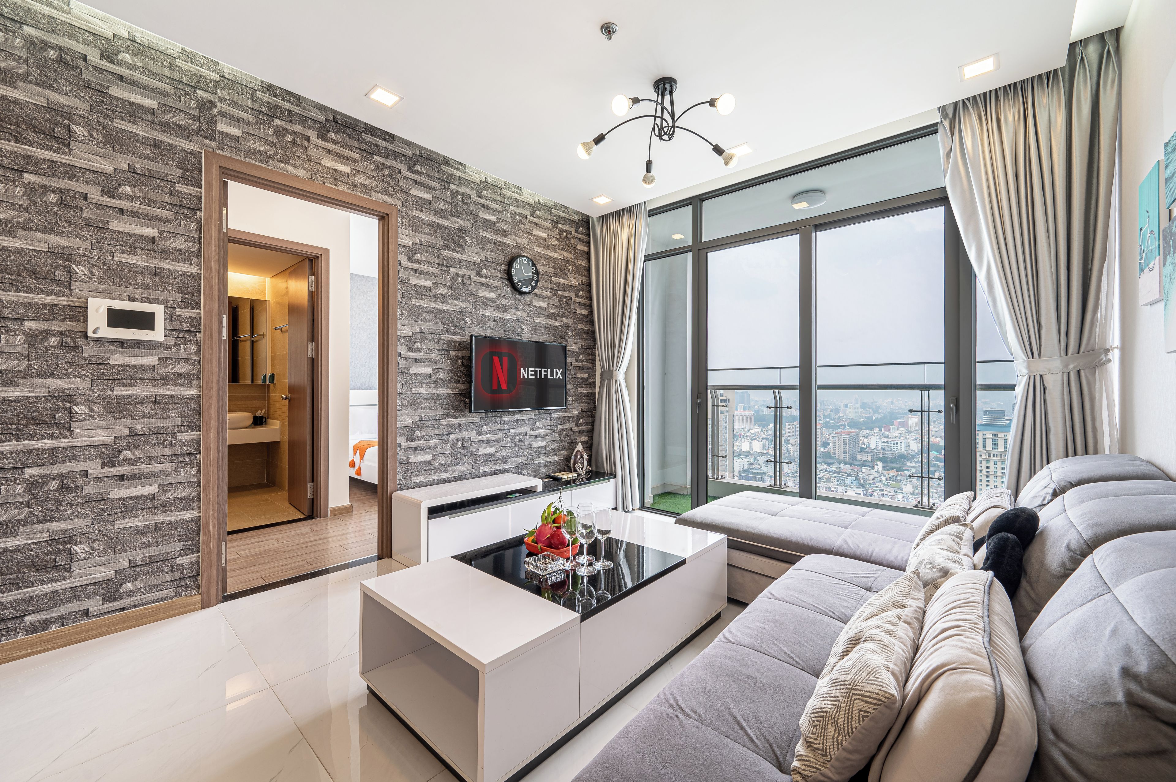 A modern living room with a sofa, a coffee table, a TV, and a large window with a city view.