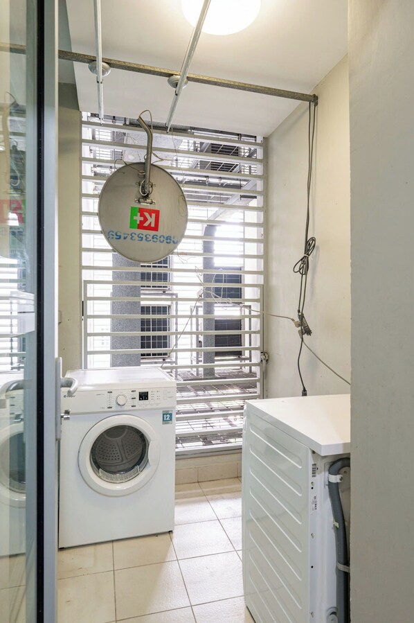 A laundry room with a washing machine, a dryer, and a window with blinds.