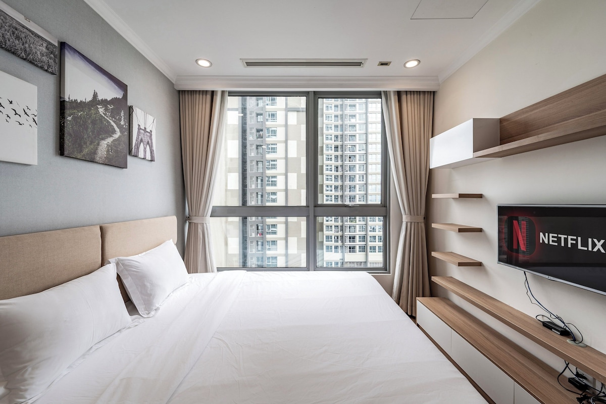 Habitación de hotel con una cama grande, un televisor montado en la pared y una ventana con vistas a la ciudad.