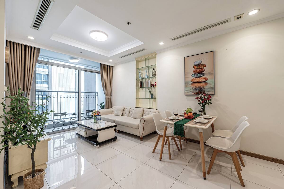 Uma sala de estar moderna com sofá, mesa de jantar, cadeiras, mesa de centro e um vaso de planta.