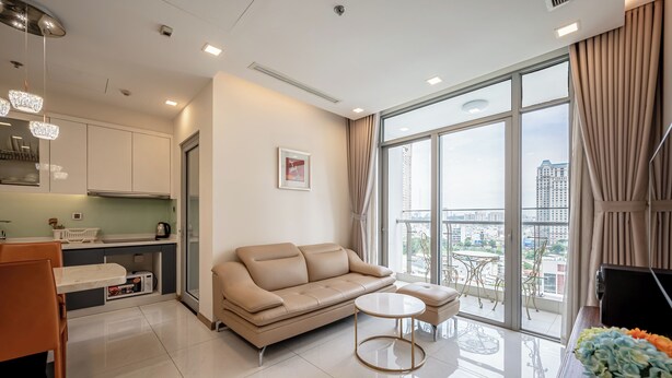 A modern living room with a sofa, coffee table, and a view of the city through large windows. - Vinhomes Central Park Apartment by Hava (Ho Chi Minh City)