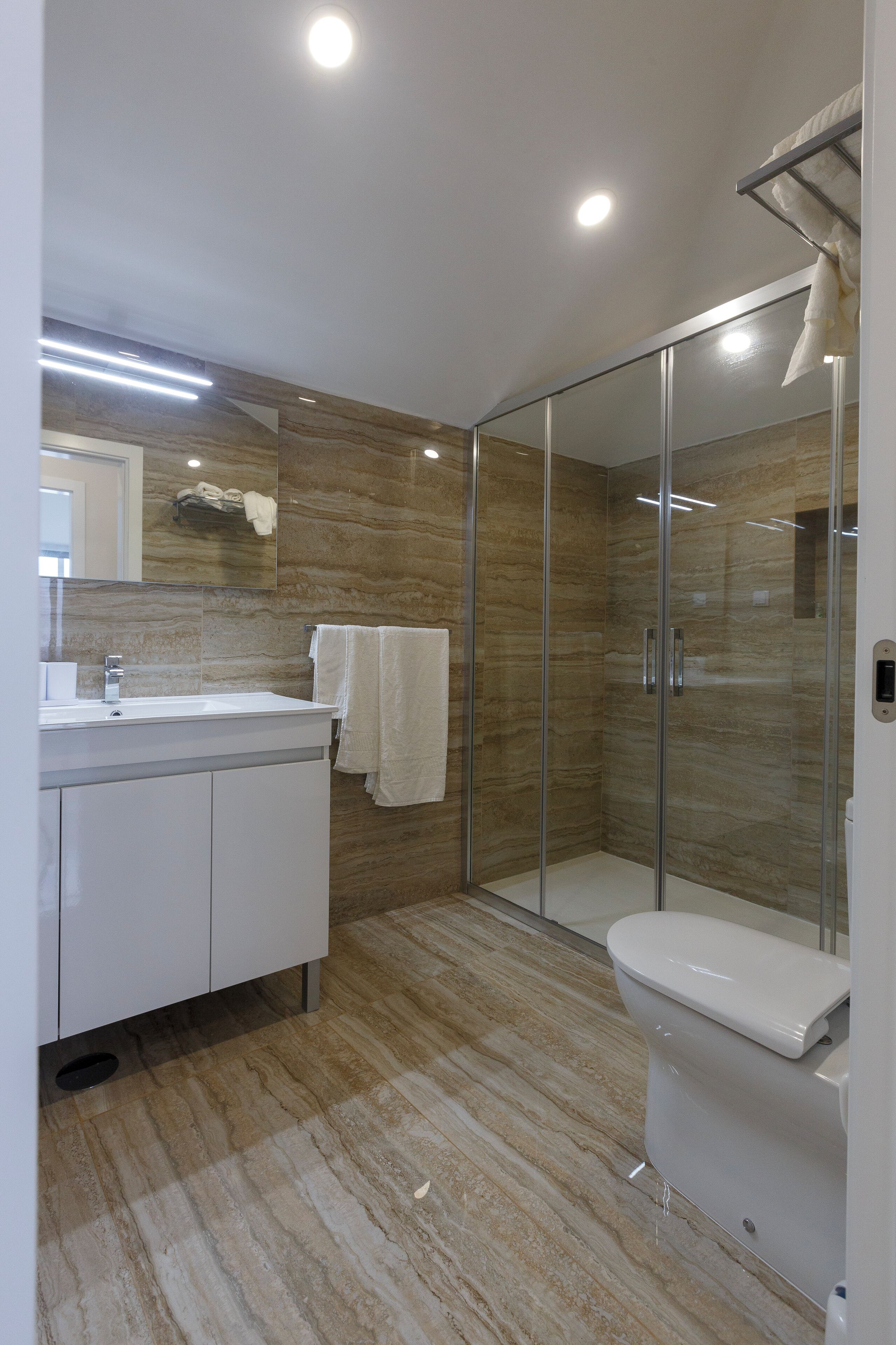 A modern bathroom with a glass-enclosed shower, a white sink, and a toilet.