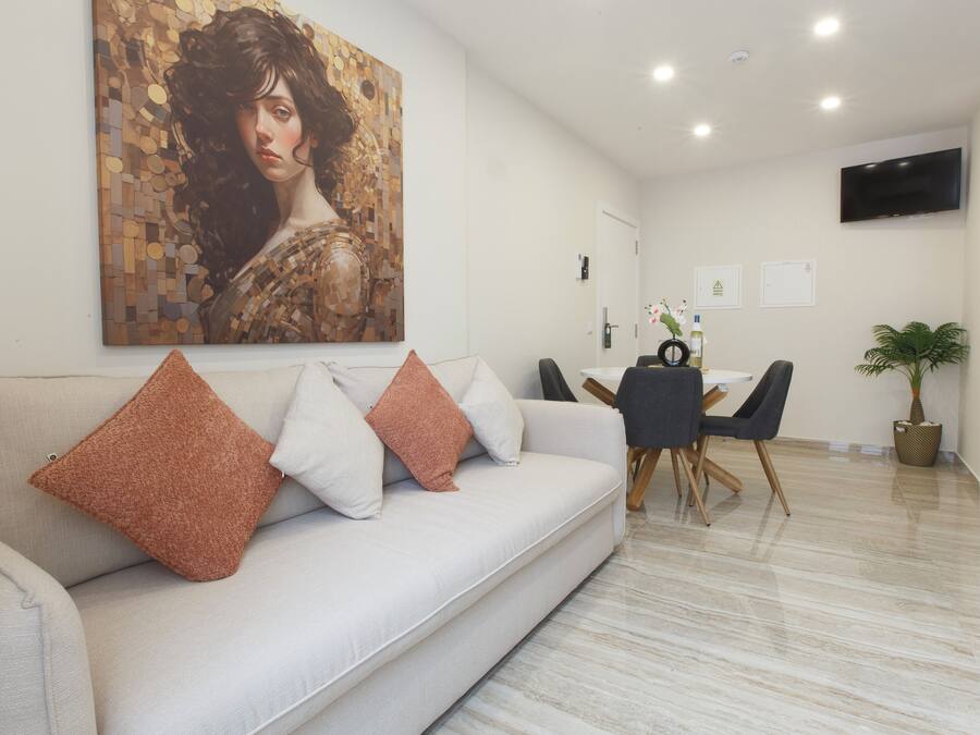A modern living room with a sofa, a dining table with chairs, a TV mounted on the wall, and a potted plant.