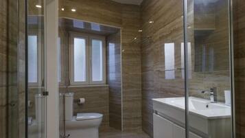 Un baño moderno con cabina de ducha de vidrio, inodoro y tocador con espejo.
