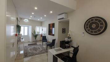 A modern office space with a desk, chairs, a large wall clock, and a potted plant.