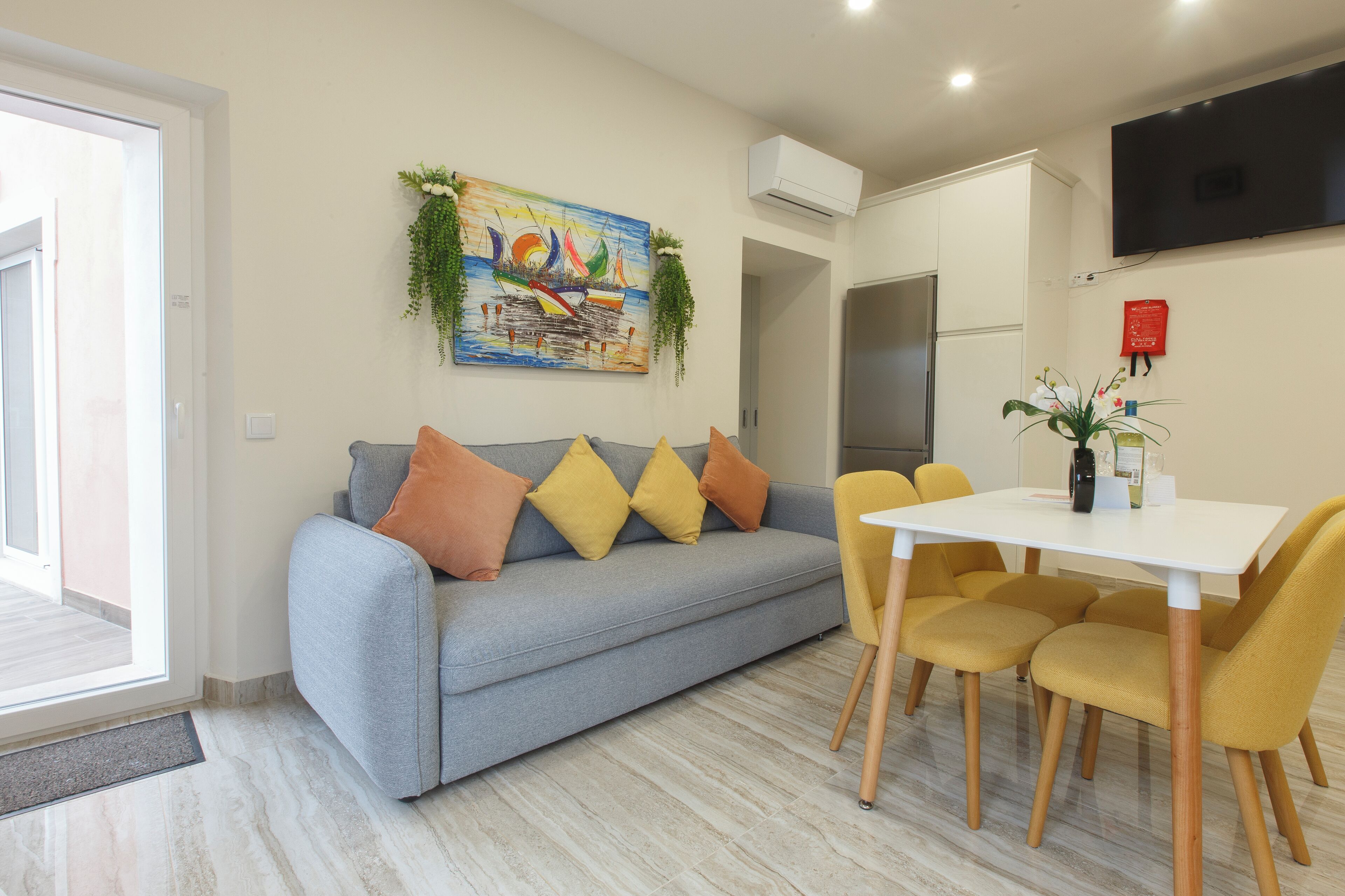 A modern living room with a grey sofa, yellow cushions, and a white dining table with yellow chairs.